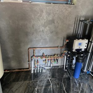 Copper and stainless steel water filtration system with multi-stage filters and pressure gauges in a modern indoor setting.