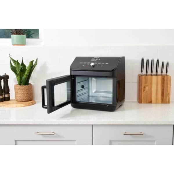 Black food dehydrator on kitchen counter with open glass door, modern design, digital control panel, ideal for health-conscious meal preparation, surrounded by kitchen utensils and plants.