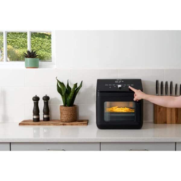 Flexible kitchen countertop with a compact black air fryer in use, surrounded by modern decor, potted plants, and kitchen accessories for a clean, stylish, and functional space.