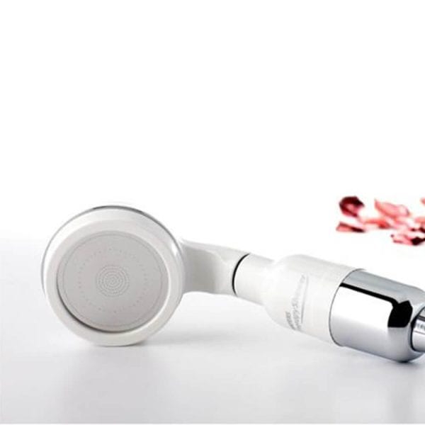 Gentle facial cleansing brush with white and silver design, perfect for skincare routines, on a white background with pink flower petals for a delicate touch.