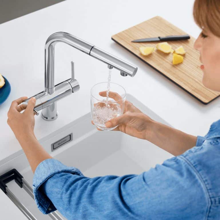 Clean drinking water being poured from a modern kitchen faucet with a water filter.